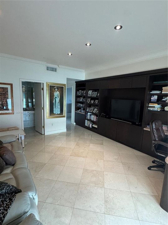 Custom dark-finish built-in shelving unit, expansive natural stone tile flooring, and recessed ceiling lighting