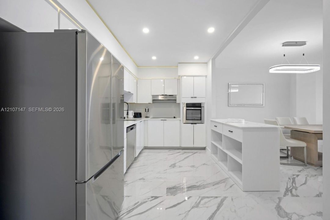 Kitchen featuring white high-gloss cabinetry, stainless steel appliances, built-in island with open shelving, recessed lighting, and large-format tile flooring