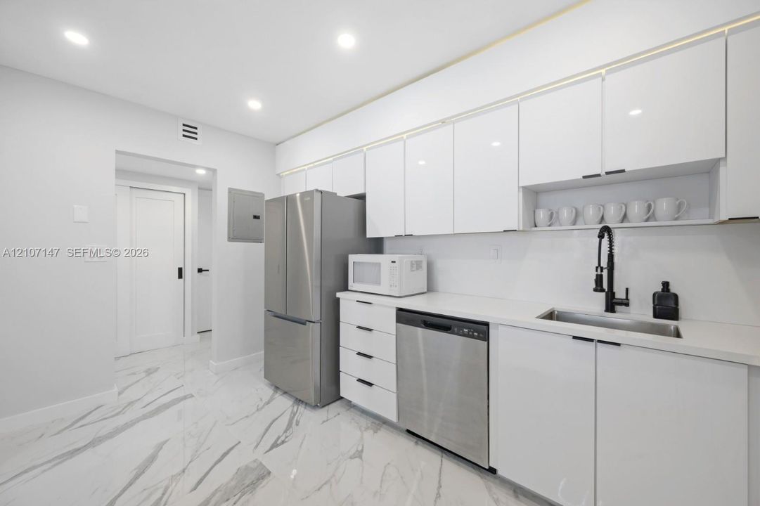 Kitchen featuring white high-gloss cabinetry, stainless steel appliances, solid-surface countertops, a matte black pull-down faucet, and polished stone-finish tile flooring