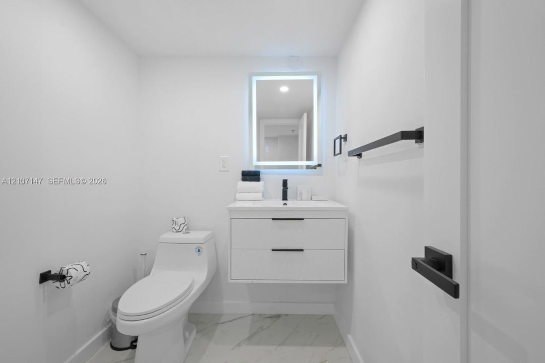 Floating vanity with integrated sink, matte black hardware, backlit rectangular mirror, and stone-finish flooring