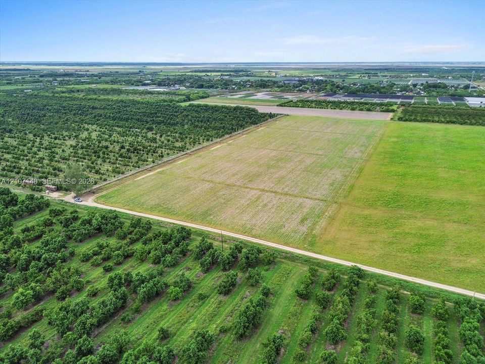 Expansive acreage featuring cultivated fields, mature orchards, and a gravel access path