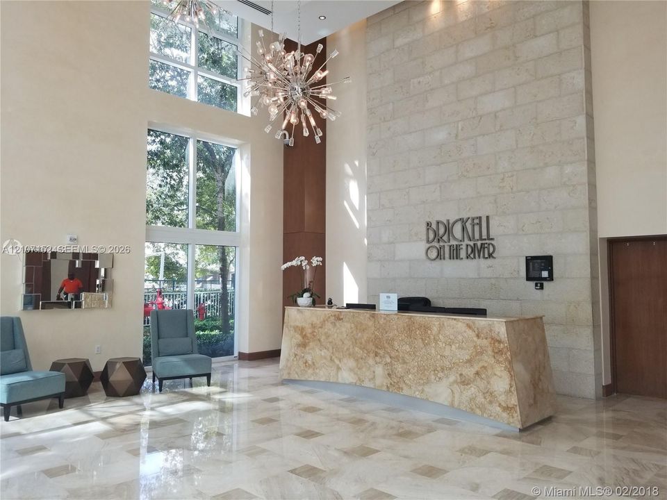 Double-height lobby featuring floor-to-ceiling windows, a stone-clad accent wall, polished stone flooring, and a bespoke stone-front reception desk