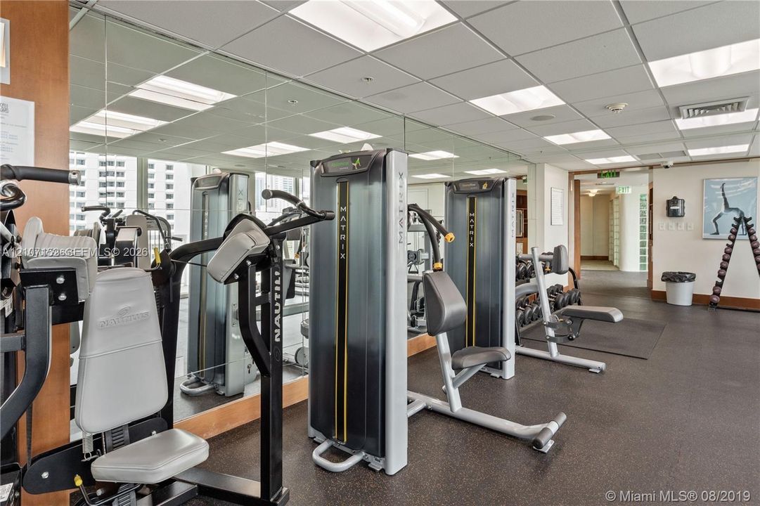 Fitness center featuring wall-to-wall mirrors, recessed grid lighting, and commercial-grade strength training equipment