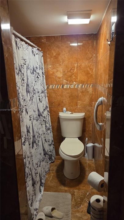 Full-height stone-finish wall tile, decorative mosaic tile inlay, wall-mounted grab bar, and flush-mount ceiling lighting