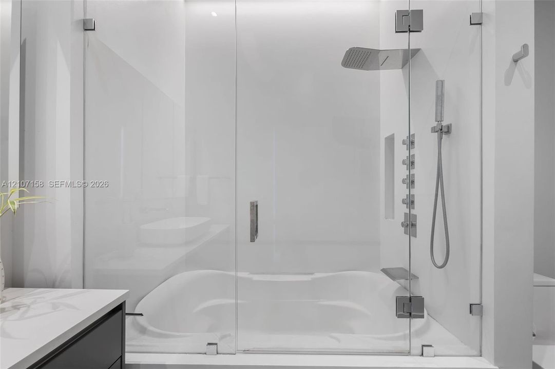 Frameless glass-enclosed shower featuring a built-in soaking tub, wall-mounted body sprays, a rectangular rainfall showerhead, and a handheld fixture