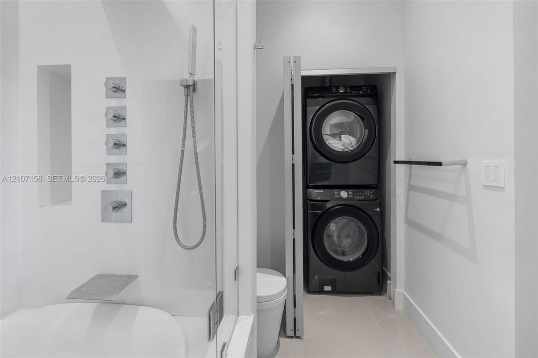 Glass-enclosed shower featuring a wall-mounted multi-head chrome rainfall system, integrated tiled shower niche, and a built-in recessed laundry closet