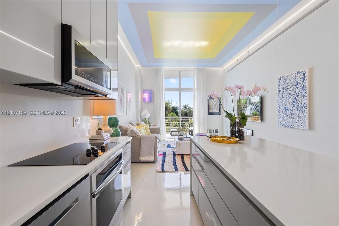 Modern kitchen featuring high-gloss cabinetry, stone-surface countertops, built-in stainless steel appliances, and a recessed ceiling design with perimeter lighting