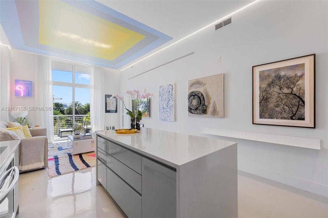Kitchen island featuring a stone countertop and handleless cabinetry, recessed ceiling lighting, and floor-to-ceiling glass door opening to a balcony