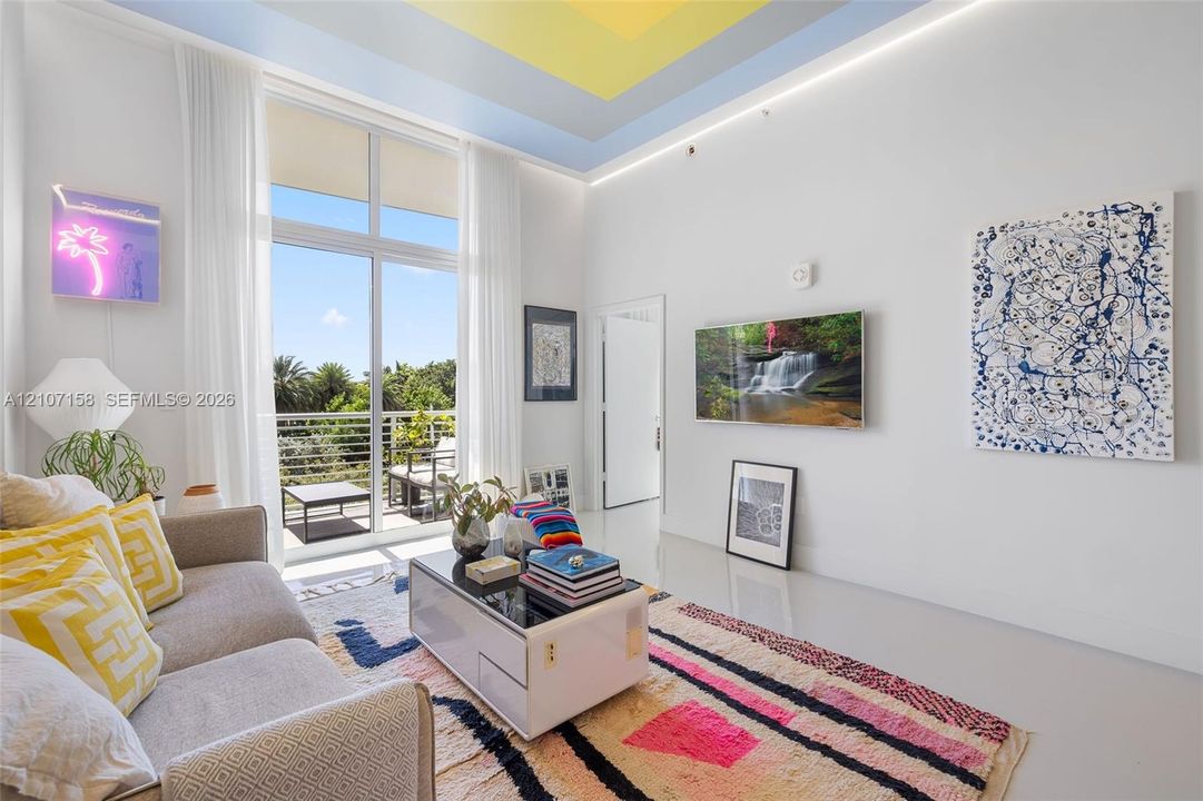 Living area featuring multi-tiered recessed ceiling detail, floor-to-ceiling windows, polished concrete flooring, recessed perimeter lighting, and a private balcony