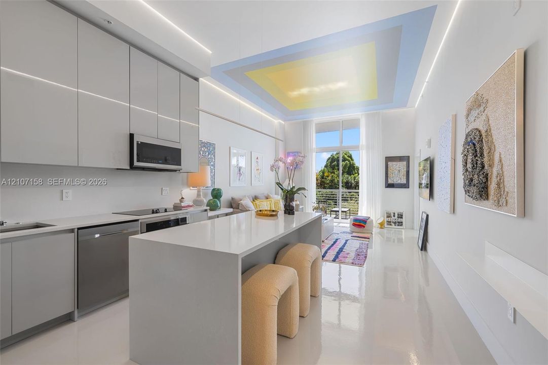 Sleek kitchen featuring flat-panel cabinetry, a waterfall-edge quartz island, stainless steel appliances, and integrated LED ceiling cove lighting