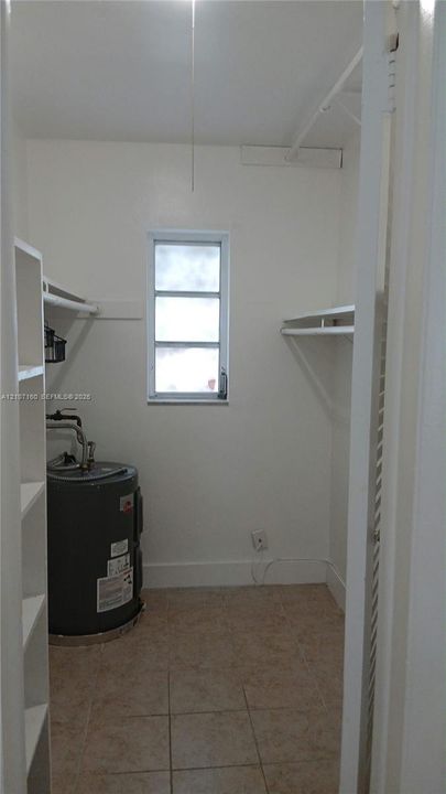 Utility room featuring tiled flooring, built-in shelving units, wall-mounted hanging rods, and a single-pane window