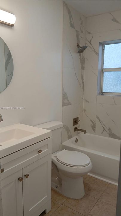 Bathroom featuring a white vanity cabinet, rectangular undermount sink, patterned wall tile surrounding the bathtub, and wall-mounted vanity lighting