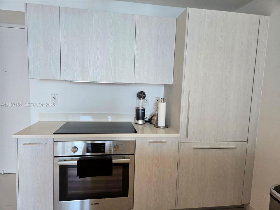 Light-toned wood-finish cabinetry, solid-surface countertops, built-in panel-ready refrigerator, and integrated stainless steel oven with a smooth-top cooktop