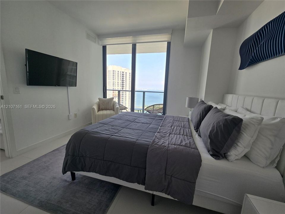 Floor-to-ceiling windows featuring roller shades, large-format tile flooring, and access to a private balcony