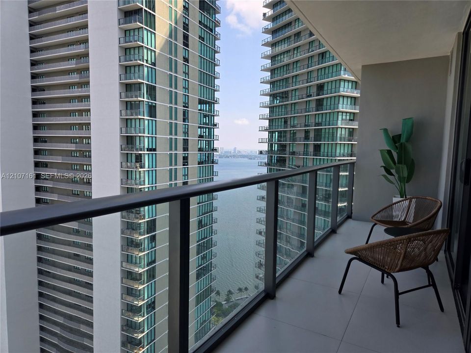 Private balcony featuring large-format tile flooring and a glass-paneled railing with a dark metal frame, overlooking an expanse of water