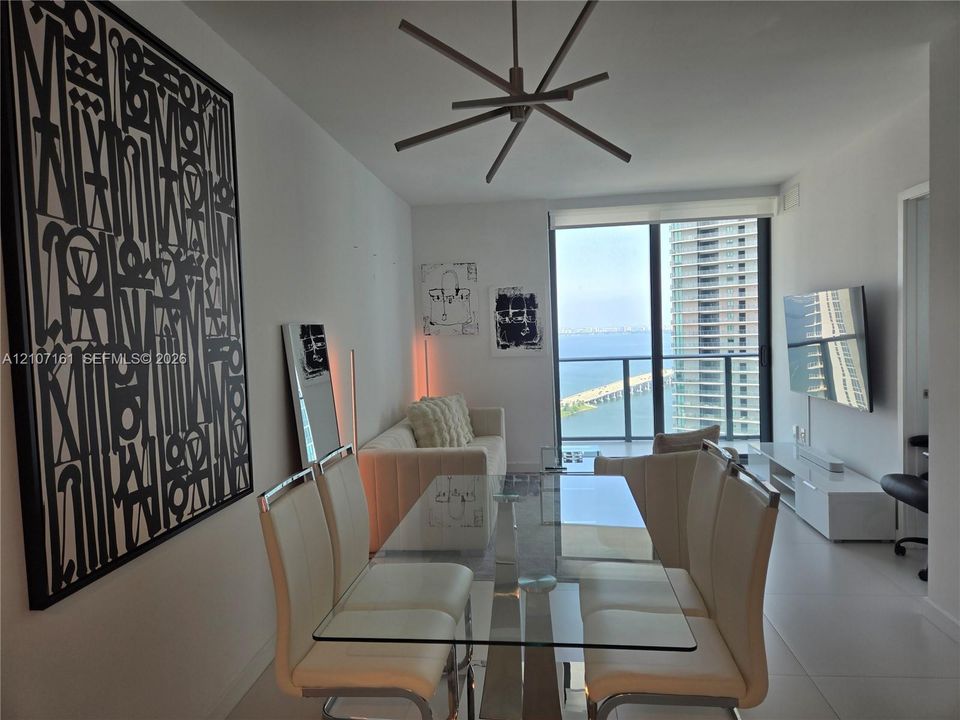 Floor-to-ceiling windows, open-concept layout, modern multi-arm chandelier, large-format tile flooring, and balcony with metal railing