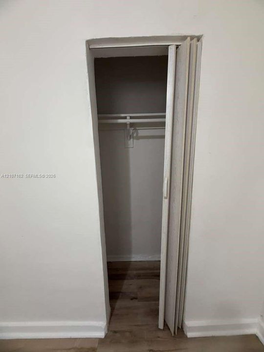 Storage closet featuring a bi-fold door, interior shelving, and a horizontal hanging rod, complemented by wood-finish flooring