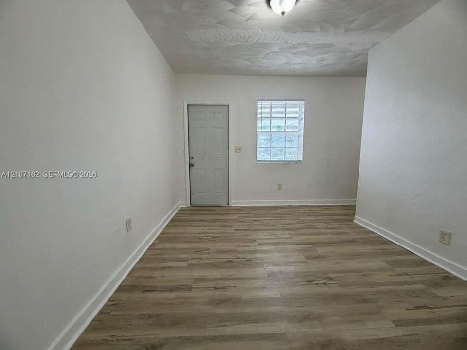 Interior space featuring wood-finish flooring, a multi-pane window, flush-mount ceiling lighting, and a six-panel door