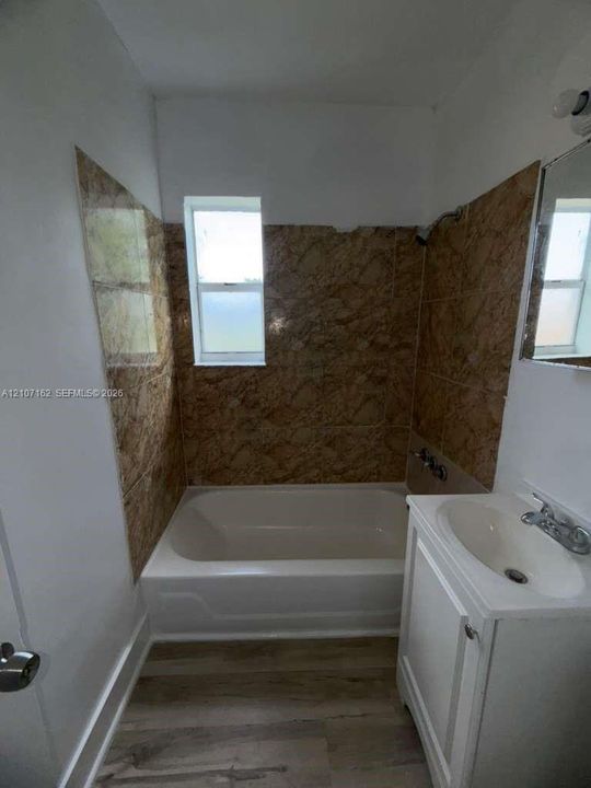 Bathroom featuring wood-finish flooring, a white vanity with an integrated sink, and a bathtub enclosure finished with patterned ceramic tile