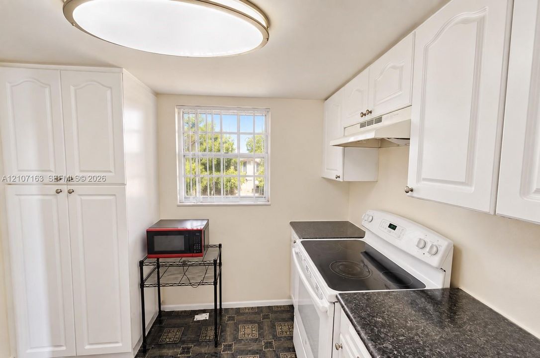 Kitchen featuring white cabinetry, dark countertops, a built-in range, and a flush-mount circular ceiling light fixture