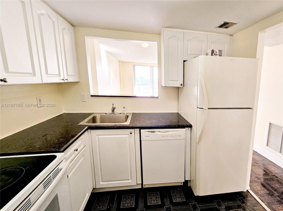 Kitchen featuring white shaker-style cabinetry, dark stone-finish countertops, stainless steel sink with a high-arch faucet, integrated dishwasher, and a full-size refrigerator