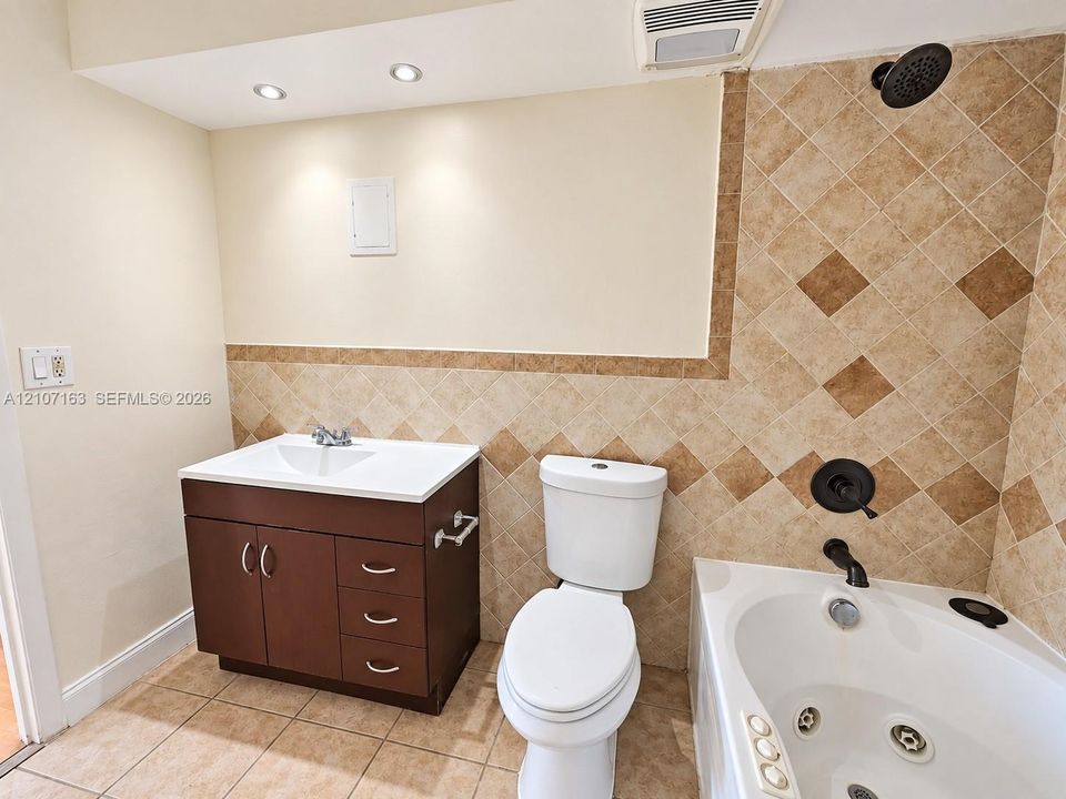 Bathroom featuring a dark wood-finish vanity with a white countertop, ceramic tile flooring, a jetted soaking tub, and stone-tile wall accents