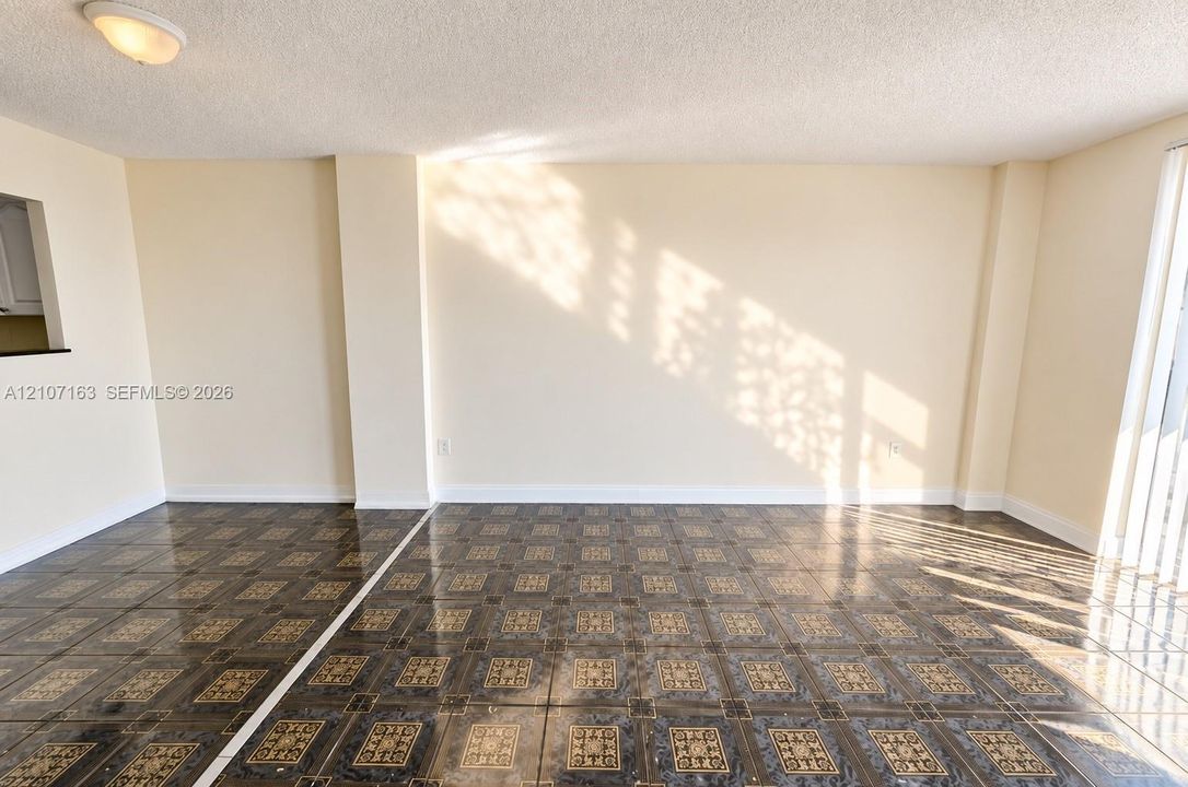 Interior space featuring patterned ceramic tile flooring, neutral wall tones, textured ceiling finish, flush-mount lighting, and a pass-through wall opening