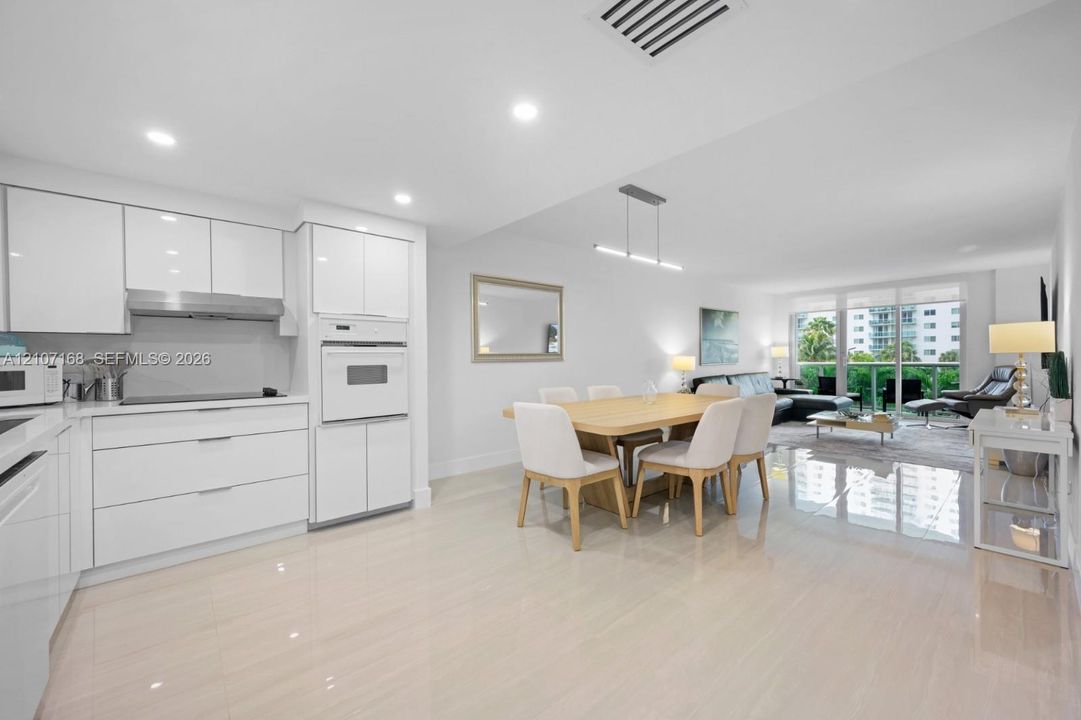 Modern kitchen featuring high-gloss white cabinetry, integrated wall oven, sleek stainless steel range hood, recessed ceiling lighting, and polished tile flooring