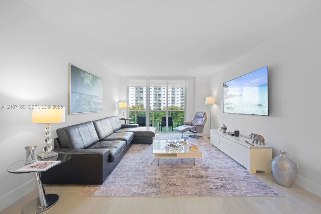 Living space featuring wood-finish flooring, floor-to-ceiling glass paneling, and access to a balcony with metal railings