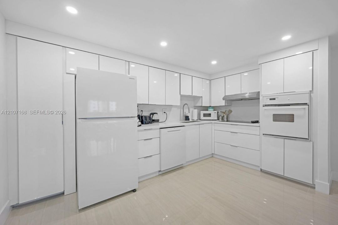 Kitchen featuring high-gloss white cabinetry, integrated white appliances, built-in wall oven, recessed lighting, and tile flooring