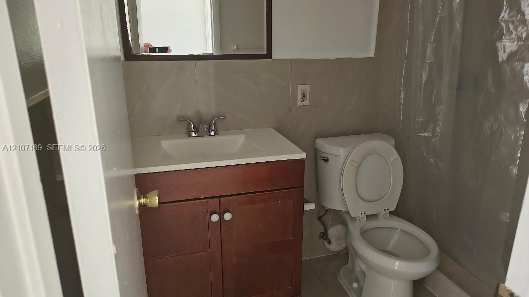 Wood-finish vanity cabinet, integrated sink with dual-handle faucet, wall-mounted mirror, and tile wall surround