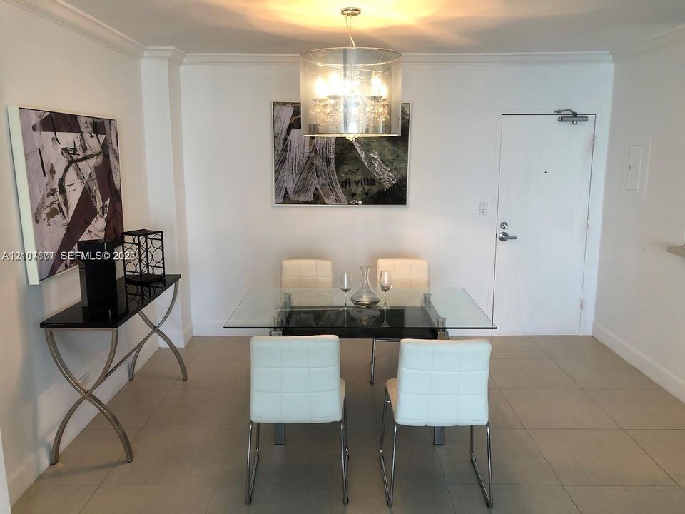 Neutral-toned tile flooring, drum-style chandelier with metallic finish, crown molding, and solid-core entry door