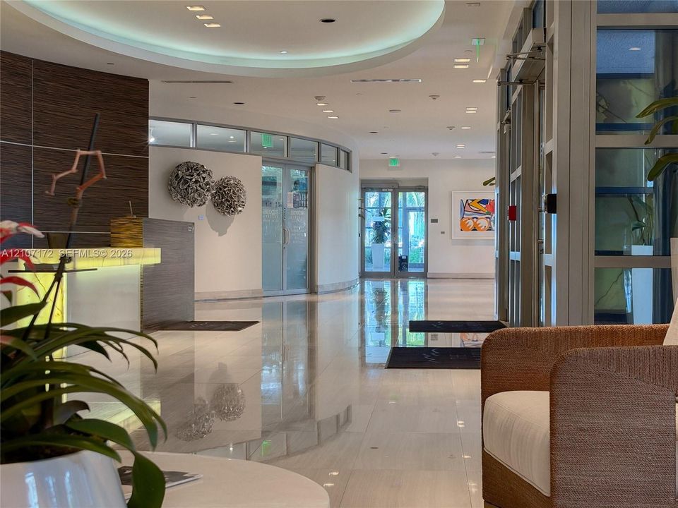 Lobby featuring polished stone flooring, recessed ceiling lighting, a curved architectural wall, and a built-in reception desk with illuminated stone-finish surfacing