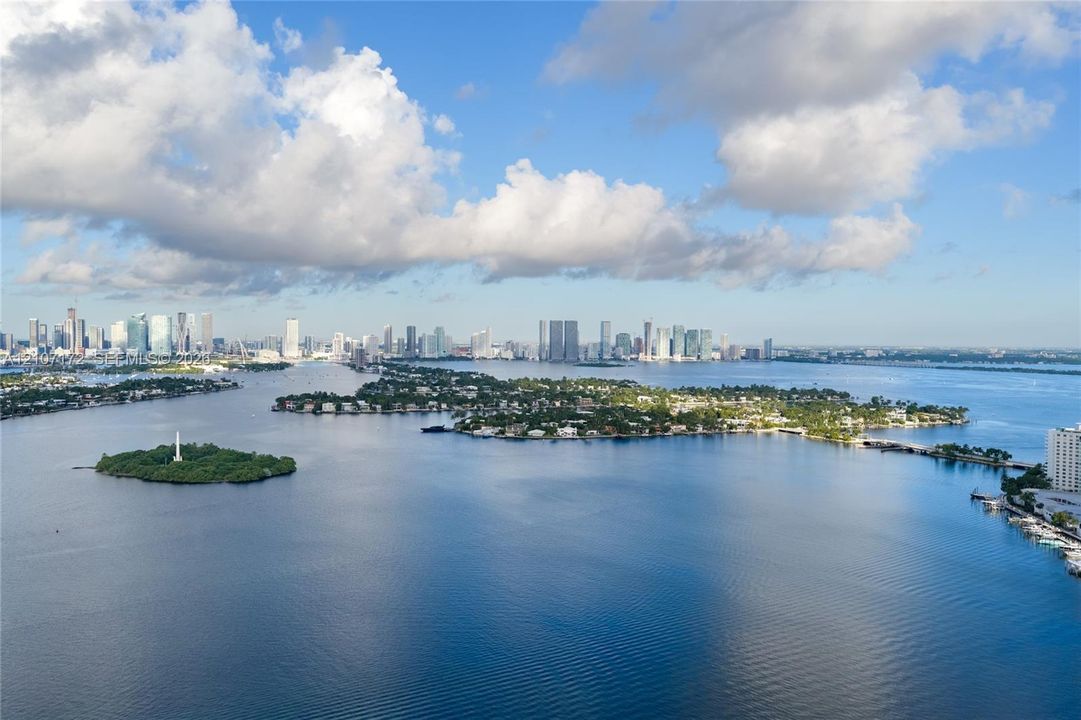 Aerial perspective featuring a sprawling coastal waterway, islands with residential landscaping, and a distant metropolitan skyline