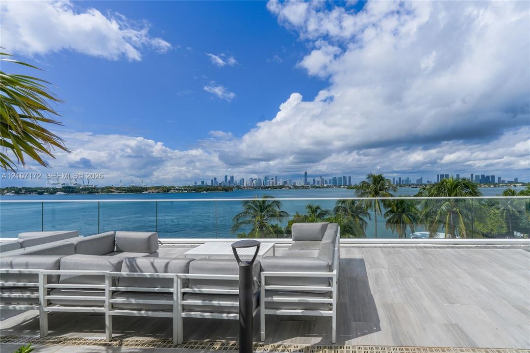 Expansive terrace featuring wood-finish tile flooring and a minimalist glass railing overlooking the water and city skyline