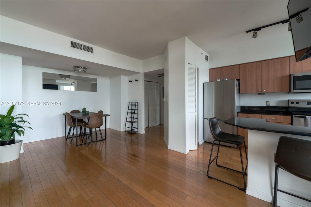 Wood-finish flooring, kitchen with dark stone-finish countertops, stainless steel appliances, track lighting, and built-in wall mirror