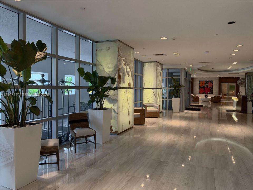 Lobby interior featuring full-height glass windows, backlit stone-clad pillars, polished stone flooring, and recessed ceiling lighting