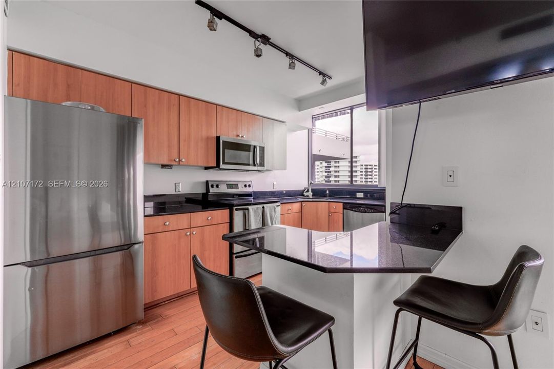Kitchen featuring wood cabinetry, stainless steel appliances, dark stone-finish countertops, a breakfast bar, and track lighting