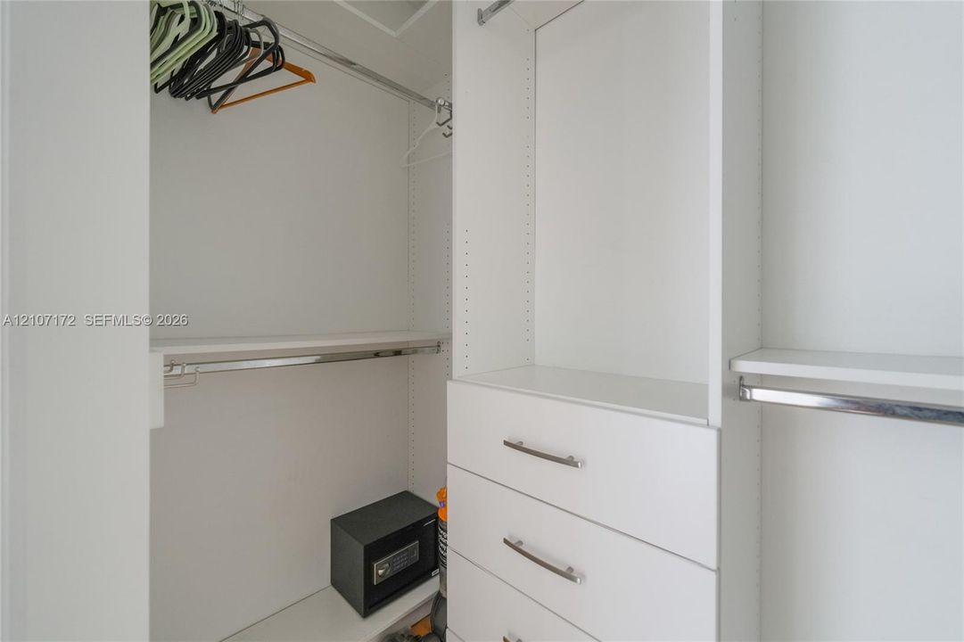 Built-in closet system featuring white cabinetry, integrated shelving, tiered hanging rods, and a stack of three drawers with metallic hardware