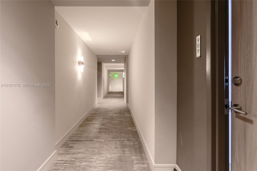 Interior hallway featuring neutral walls, wall-mounted sconce lighting, and textured carpeting