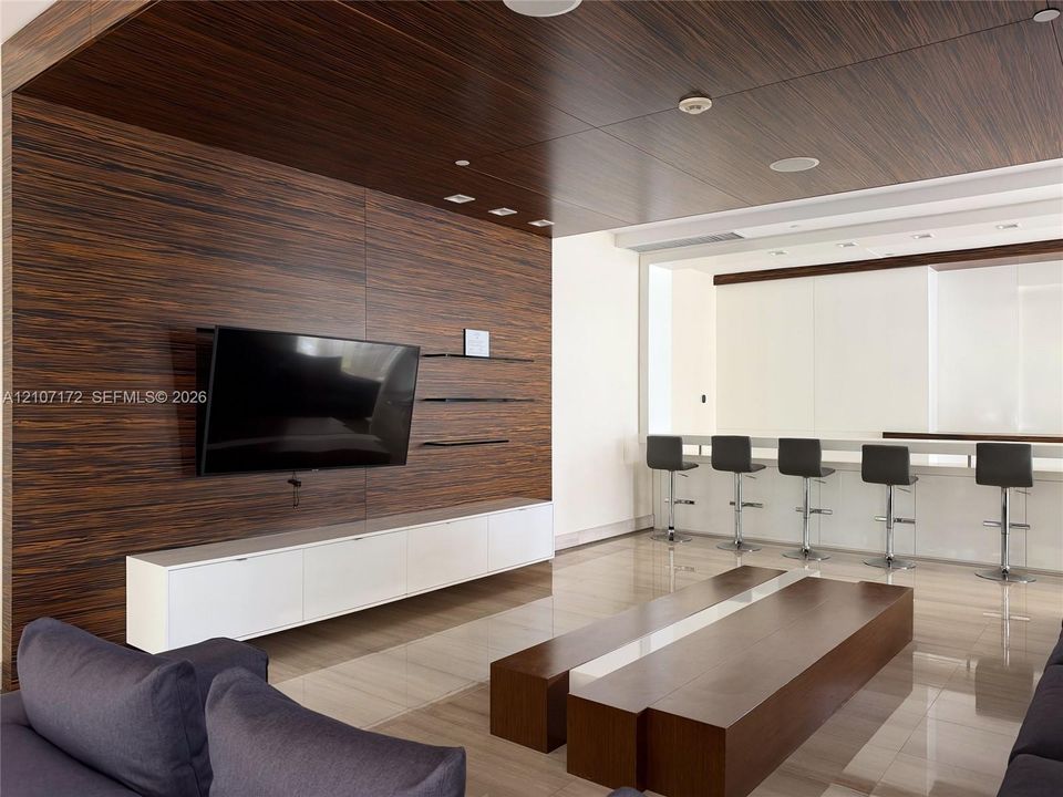 Floor-to-ceiling dark wood-finish paneling with integrated wall shelving, white lacquer built-in cabinetry, polished stone flooring, and a sleek breakfast bar with high-gloss cabinetry