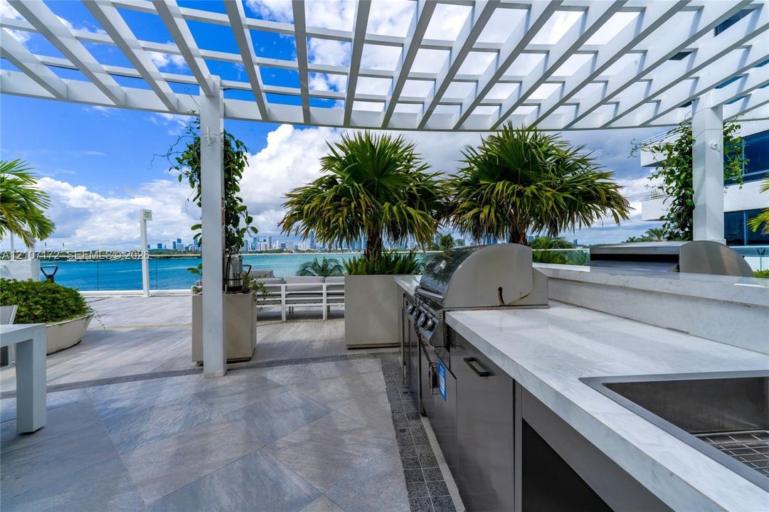 Outdoor terrace featuring a white pergola, stainless steel built-in grill, stone-surface countertop, and large planters
