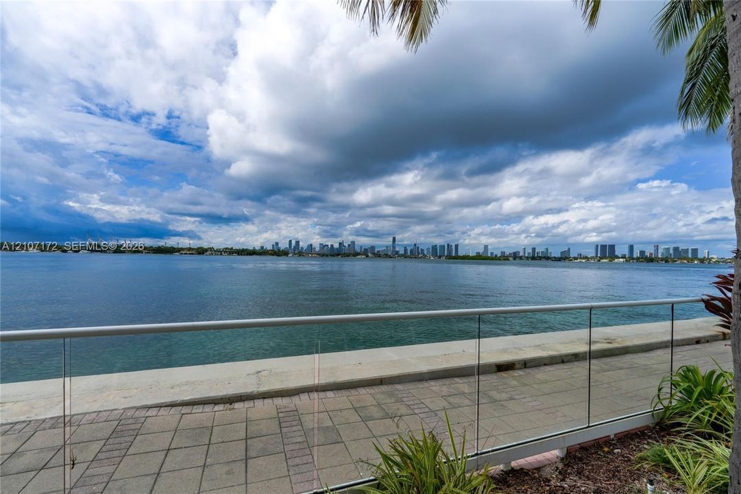 Waterfront patio featuring a paved stone terrace, glass panel railing, and cityscape backdrop