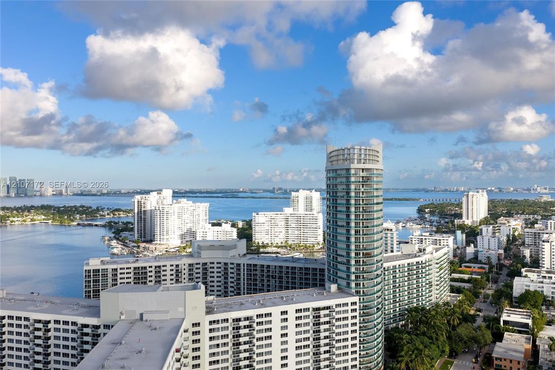 Aerial perspective featuring a glass-facade high-rise tower, expansive coastal waterfront, and urban skyline