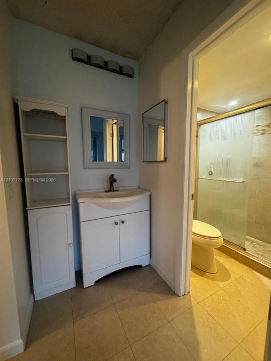 Bathroom featuring a white vanity cabinet, built-in floor-to-ceiling storage unit, tile flooring, and a walk-in shower with a glass enclosure