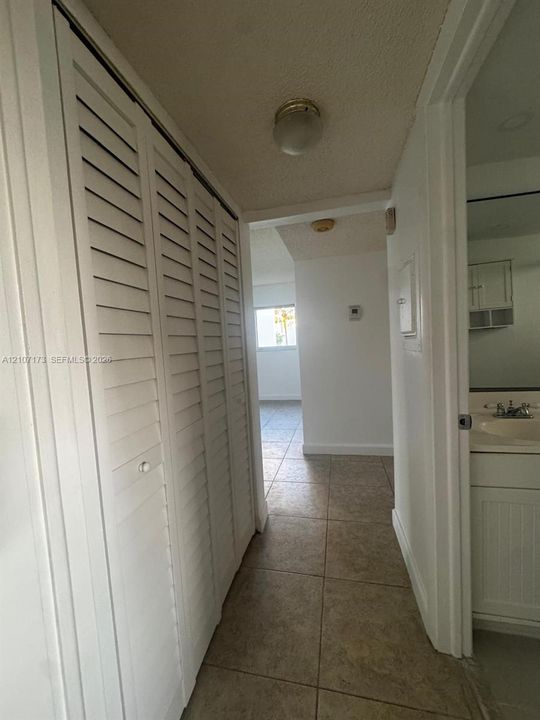 Hallway featuring full-height bi-fold louvered closet doors, neutral stone-finish tile flooring, and a vanity cabinet with an integrated sink