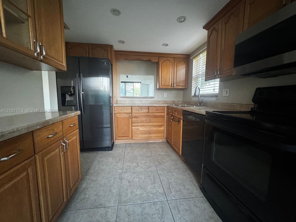 Kitchen featuring wood cabinetry, stone-finish countertops, tile flooring, recessed lighting, and integrated black appliances