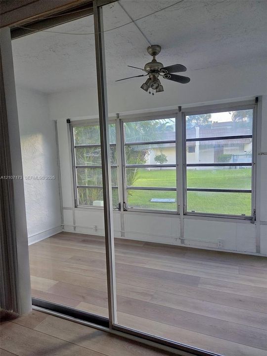 Wood-finish flooring, floor-to-ceiling mirror paneled closet doors, expansive multi-pane windows, and a multi-blade ceiling fan with integrated lighting