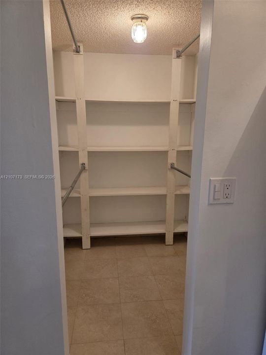Walk-in storage space featuring custom multi-level shelving, integrated hanging rods, tiled flooring, and a flush-mount light fixture