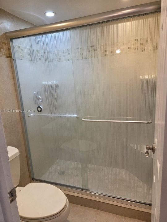 Shower enclosure featuring a sliding glass door with textured finish, integrated corner shelving, stone-tiled wall surrounds with a mosaic accent border, and recessed ceiling lighting